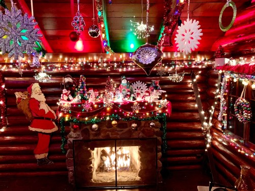 Cozy cabin interior decorated for Christmas, featuring a fireplace, colorful lights, and festive ornaments.