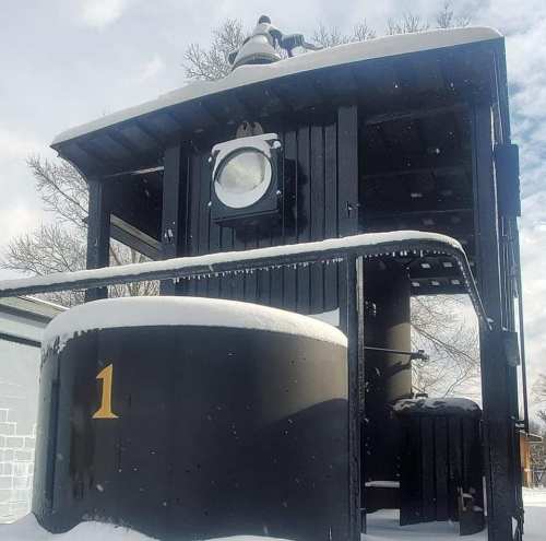 A black train engine covered in snow, featuring a large circular window and the number 1 displayed prominently.