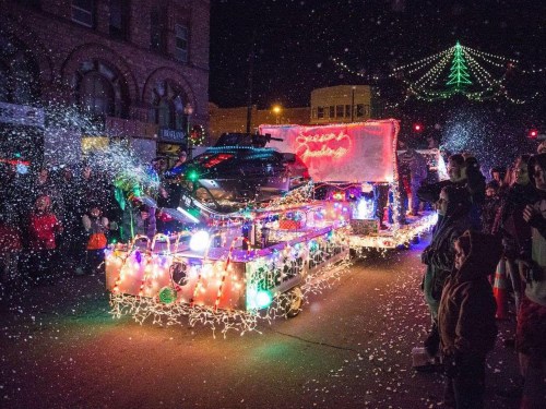 A festive parade float adorned with colorful lights and decorations, surrounded by snow and onlookers at night.