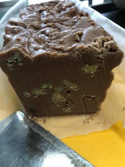 A close-up of a chocolate fudge block with visible nuts, resting on parchment paper with a knife beside it.