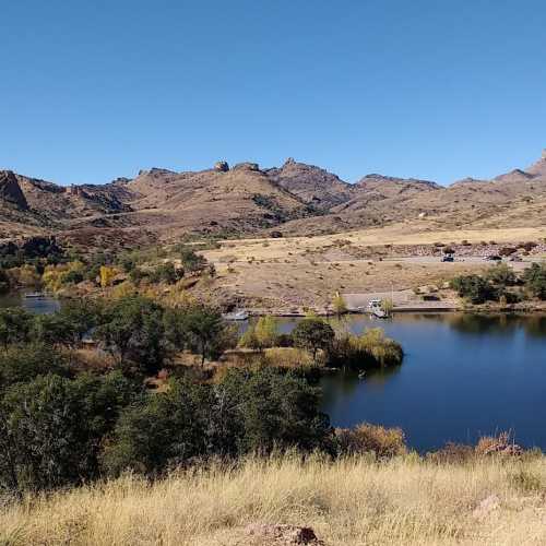 A serene landscape featuring a calm river surrounded by hills and trees under a clear blue sky.