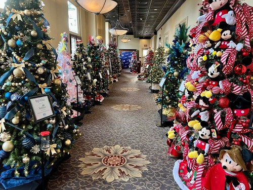 A festive hallway lined with decorated Christmas trees, featuring colorful ornaments and themed decorations.