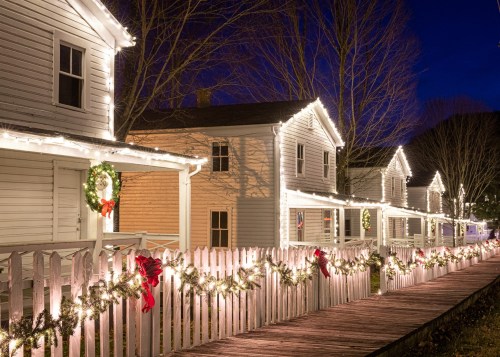 Charming houses adorned with festive lights and decorations along a wooden walkway at night.