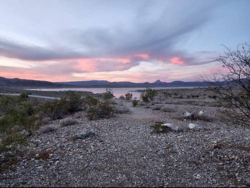 A serene landscape at dusk, featuring a lake, distant mountains, and a colorful sky with pink and purple hues.