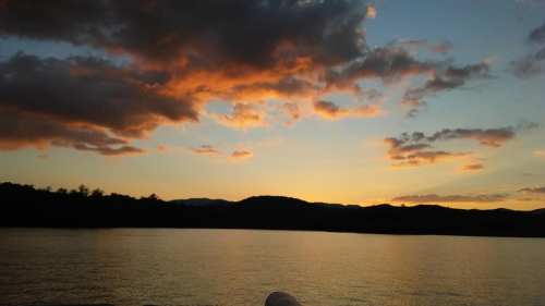 A serene sunset over a calm lake, with colorful clouds reflecting on the water and mountains in the background.