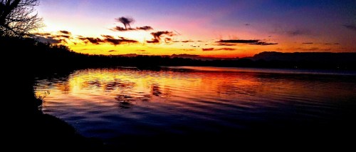 A serene sunset over a calm lake, with vibrant orange and purple hues reflecting on the water's surface.