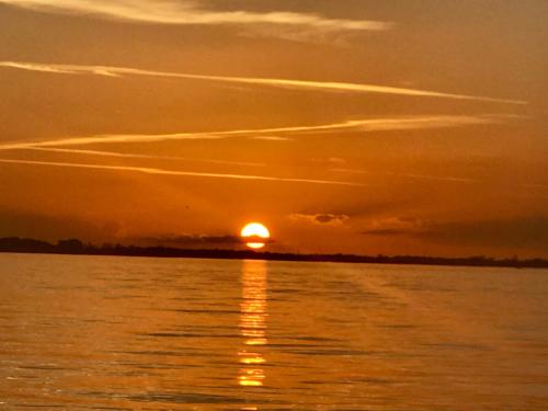 A serene sunset over calm waters, with vibrant orange hues and soft clouds reflecting on the surface.