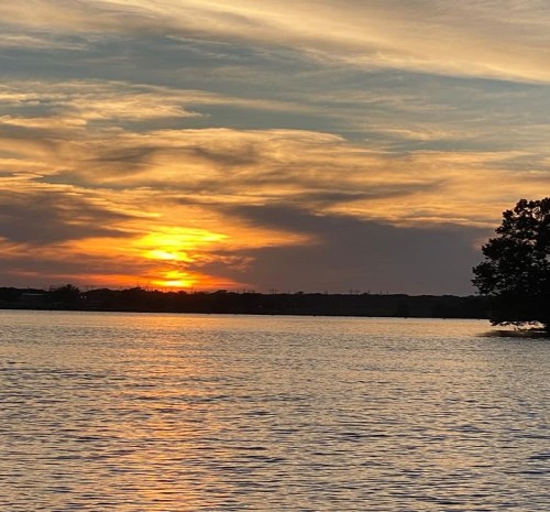 A serene sunset over a calm lake, with vibrant orange and yellow hues reflecting on the water and clouds.