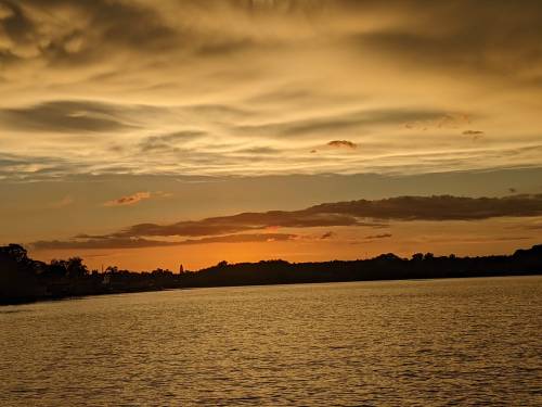 A serene sunset over a calm lake, with golden and orange hues reflecting on the water and clouds in the sky.