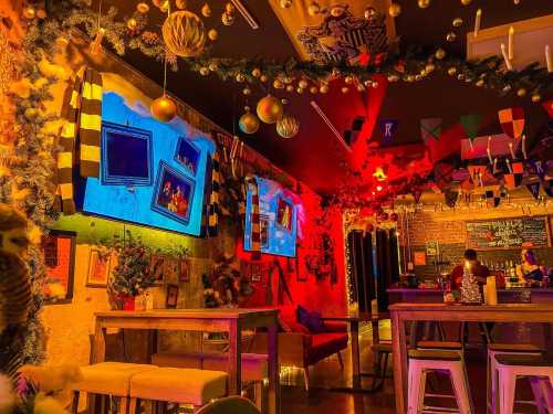 A vibrant bar interior decorated with festive lights, colorful banners, and screens displaying images on the walls.