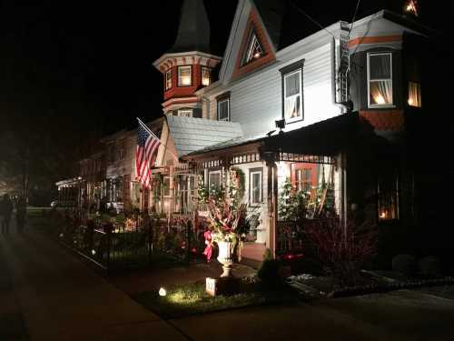 A beautifully lit Victorian-style house decorated for the holidays, featuring an American flag and festive greenery.