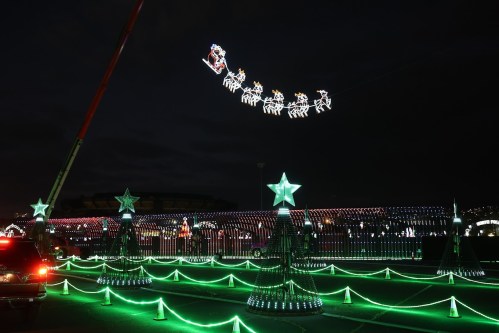 Colorful holiday lights display featuring reindeer and sleigh, with decorated trees and stars against a night sky.