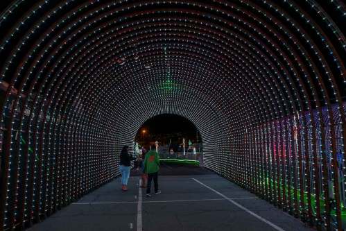A colorful light tunnel with people walking through, illuminated by vibrant LED lights in various patterns.