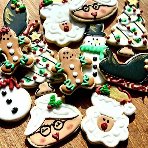 A variety of decorated holiday cookies, including gingerbread men, snowmen, and Christmas trees, on a wooden surface.