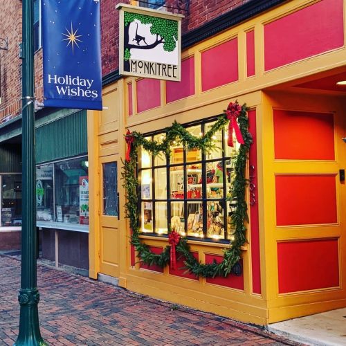 A colorful storefront decorated with holiday wreaths and ribbons, with a "Holiday Wishes" banner nearby.