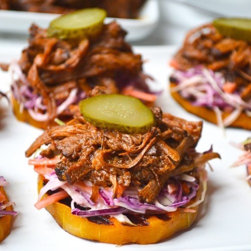 Pulled beef on sweet potato rounds, topped with coleslaw and pickles, served on a white platter.