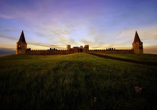 A medieval castle with two towers, set on a grassy hill under a colorful sunset sky.