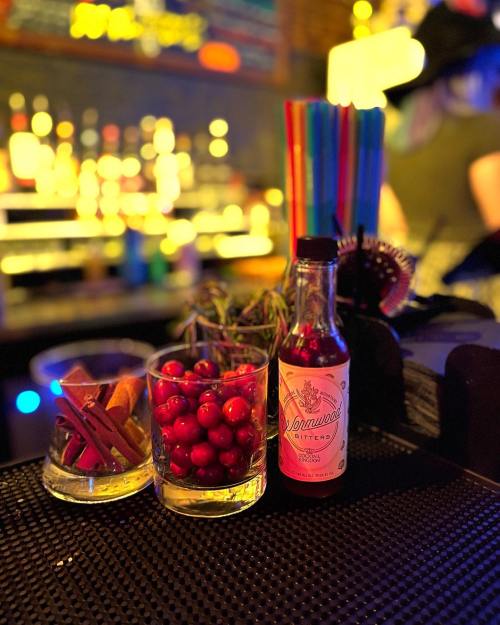 A vibrant bar scene featuring glasses of cherries and cinnamon sticks, a bottle of syrup, and colorful straws in the background.