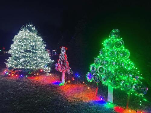 Three Christmas trees: one sparkling white, one made of hubcaps, and a smaller red tree, all illuminated with colorful lights.