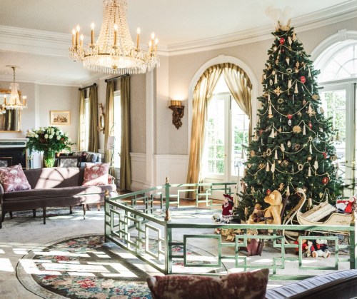 A beautifully decorated living room featuring a large Christmas tree, elegant furnishings, and festive decorations.