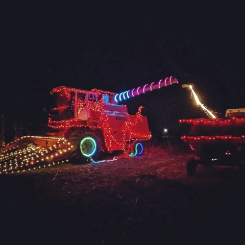 A brightly lit tractor decorated with colorful lights, featuring a large, illuminated cannon on top, set in a dark field.