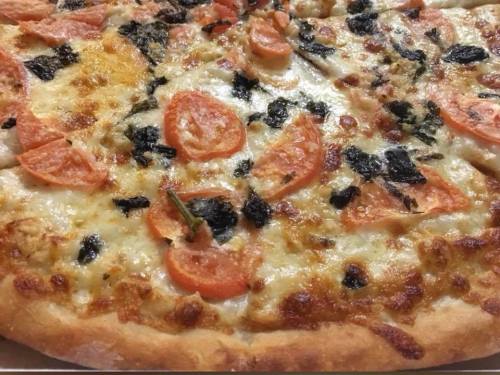 Close-up of a pizza topped with melted cheese, sliced tomatoes, and dark leafy greens.