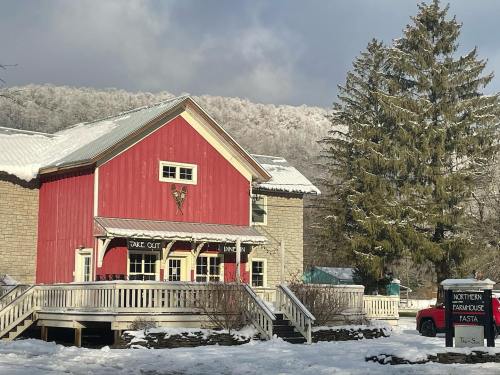 A red farmhouse with a stone exterior, surrounded by snow and trees, featuring a sign for takeout and dining.
