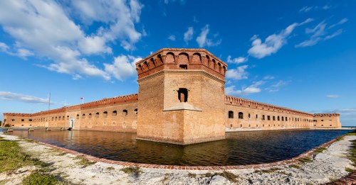Historic brick fort surrounded by water, with a clear blue sky and clouds in the background.