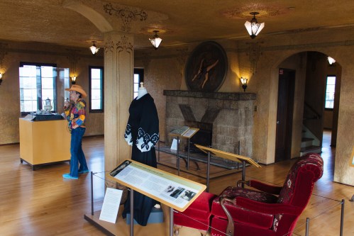 A museum interior featuring a display of artifacts, a chair, and a visitor in colorful attire.