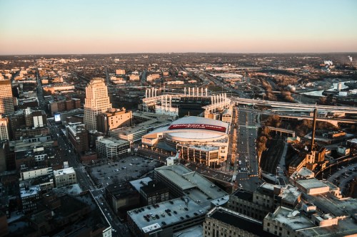 Aerial view of a cityscape at sunset, featuring stadiums, buildings, and roads.