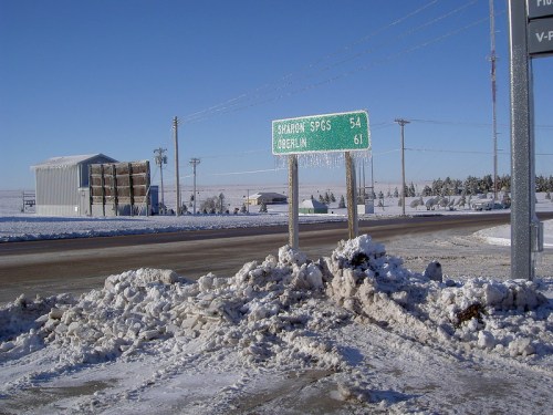 Snowy roadside sign indicating distances to Sharlow Springs (54 miles) and Greenlin (61 miles) with a snowy landscape.