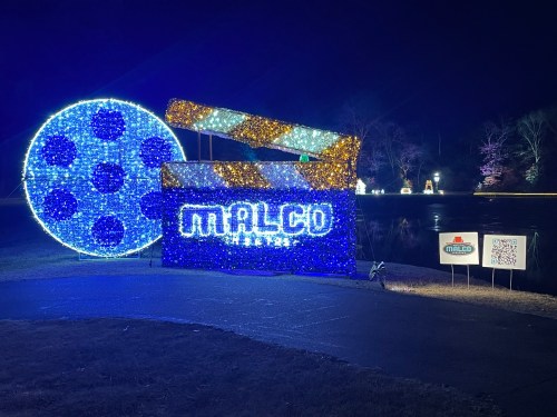 A colorful light display featuring a film clapperboard and a large film reel by a pond at night.