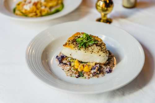 A beautifully plated dish featuring a piece of fish on a bed of colorful grains and vegetables, garnished with herbs.