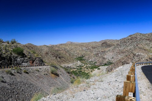 A scenic view of a desert landscape with mountains, a clear blue sky, and a winding road along the edge.