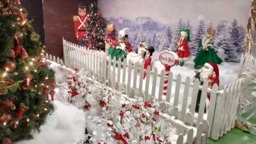 A festive winter scene with a white picket fence, Christmas trees, and holiday decorations, featuring animated figures.