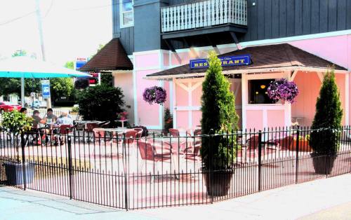 Outdoor restaurant patio with tables and chairs, surrounded by a black fence and colorful flower arrangements.
