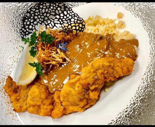 A plate of fried chicken with a rich sauce, garnished with herbs, lemon, and crispy noodles.