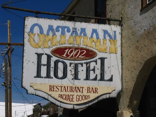 Sign for the Oatman Hotel, established in 1902, featuring a restaurant, bar, and package goods. Weathered and vintage look.