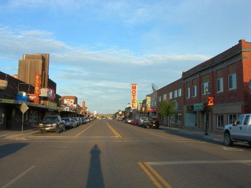 A quiet street scene featuring shops, a motel sign, and parked cars under a clear blue sky.