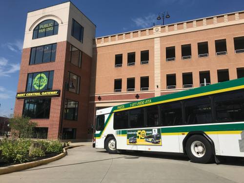 A public bus parked in front of a modern building with a sign for public parking and the Kent Central Gateway.