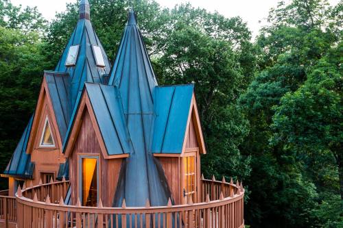 A unique wooden house with pointed roofs, surrounded by trees and featuring a circular balcony.