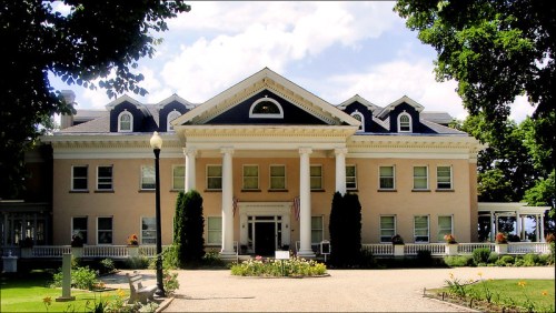 A large, elegant building with a classic facade, featuring columns, a porch, and landscaped gardens.