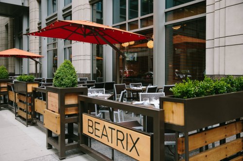 Outdoor dining area of a restaurant named "Beatrix," featuring tables, chairs, and red umbrellas.