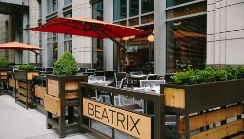 Outdoor dining area of a restaurant named Beatrix, featuring tables, chairs, and red umbrellas.