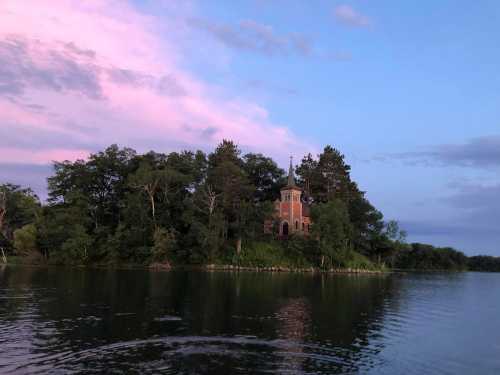 A serene lake scene at sunset, featuring a small island with a brick building surrounded by trees and colorful clouds.