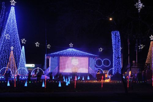 Colorful holiday lights illuminate a park with a large screen displaying a festive scene at night.