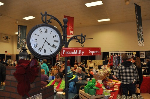 A clock and sign for Piccadilly Square in a bustling indoor market filled with people and various stalls.