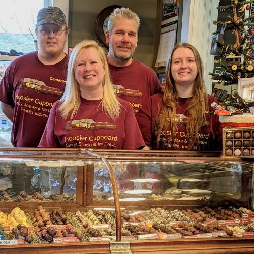 A family stands behind a display of chocolates at Hoosier Cupboard, wearing matching maroon shirts.