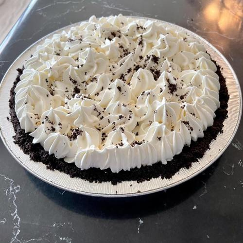A round chocolate pie with a creamy whipped topping and chocolate cookie crumbs on the edges.