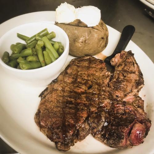 A plate featuring grilled steak, a baked potato with butter, and a side of green beans.